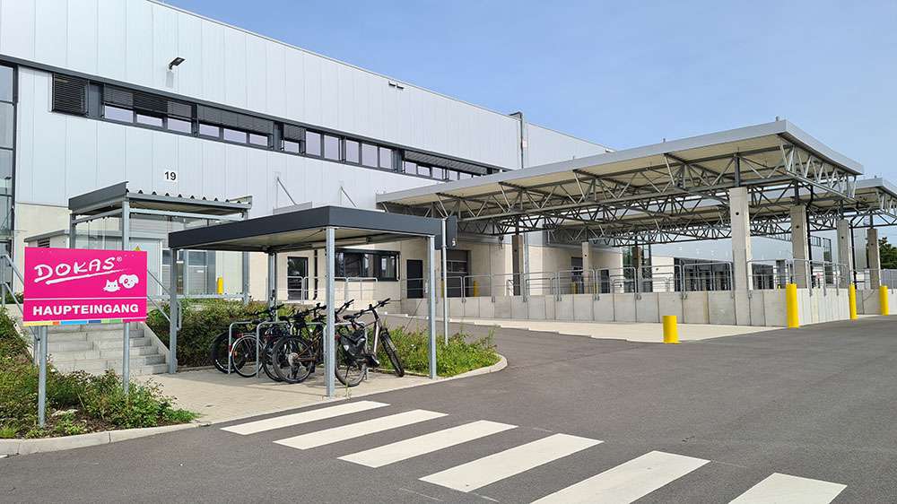 Modernes Dokas-Hauptgebäude mit Fahrradständer und „Haupteingang“-Schild.